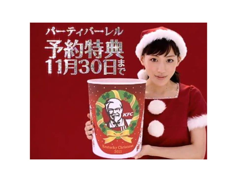 Eine Japanerin im Weihnachtsmann-Outfit hält einen Behälter der Fastfoodkette Kentucky Fried Chicken in die Kamera-