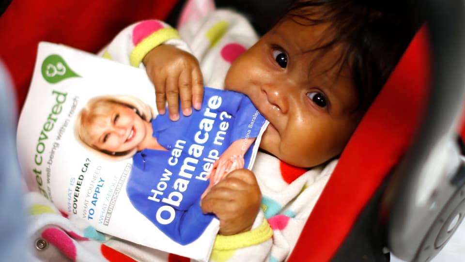 Ein Latino-Kleinkind im Wagen knabbert eine Broschüre zu «Obamacare» an.
