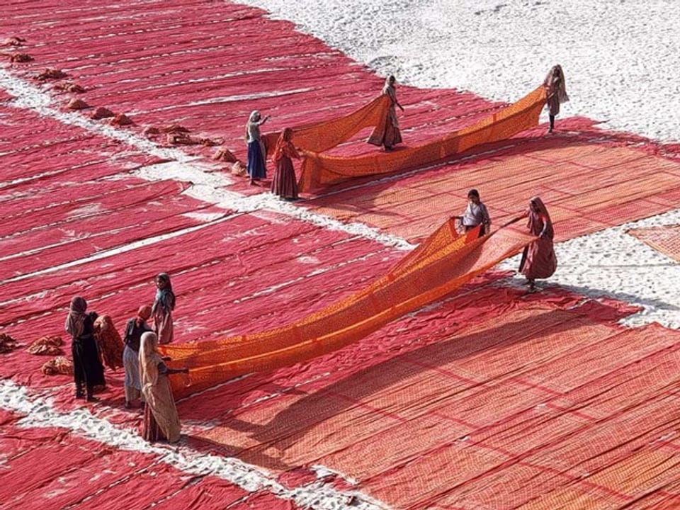 Rote Saris liegen am Boden zum Trocknen aus.