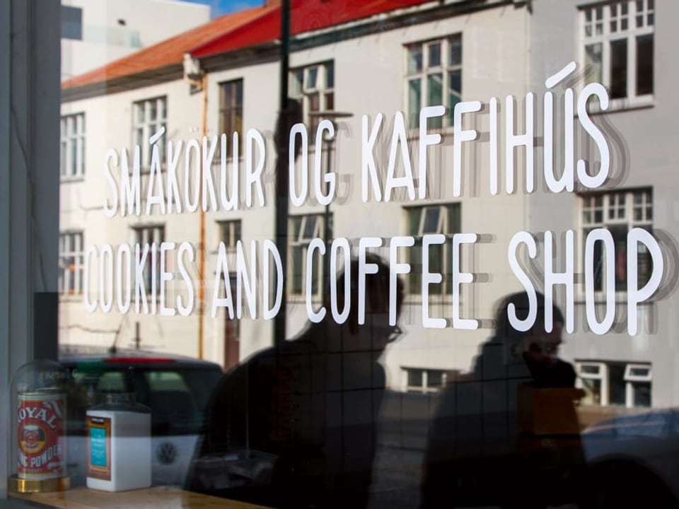 Eine Häuserzeile spiegelt sich in dem Schaufenster eines Cafés. Auf dem Fenster steht: «Cookies and Coffee Shop»