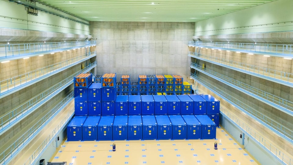 Mehrere blaue Container stehen in einer grossen Lagerhalle.