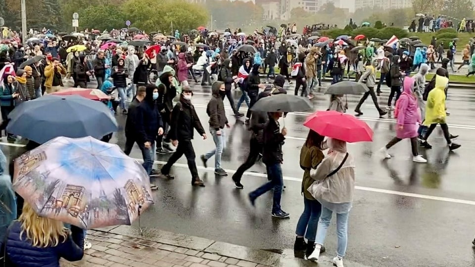 Eine Menschenmenge steht im Regen auf der Strasse.