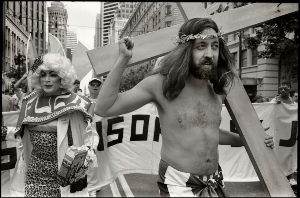 A man who looks like Jesus holds a wooden cross in pride