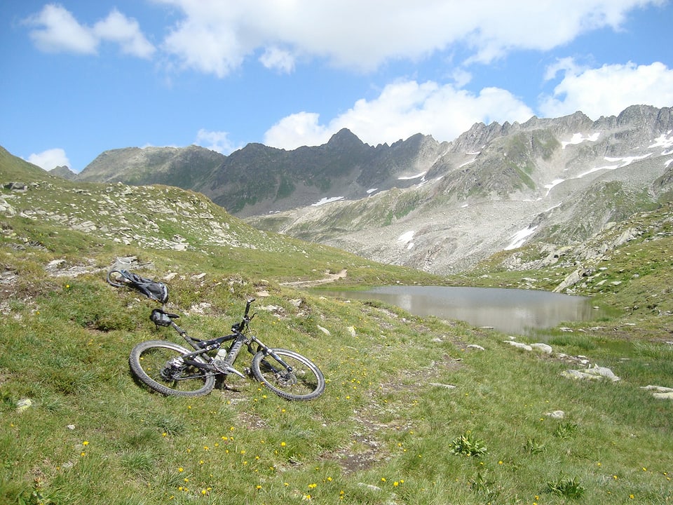 Mountainbike liegt auf einer Wiese in den Bergen im Hintergrund ein Bergsee, der Tomasee