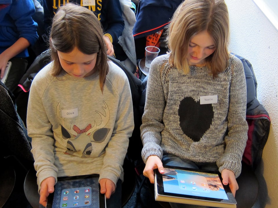 Zwei Mädchen sitzen nebeneinander und schauen auf ihre Tablets.