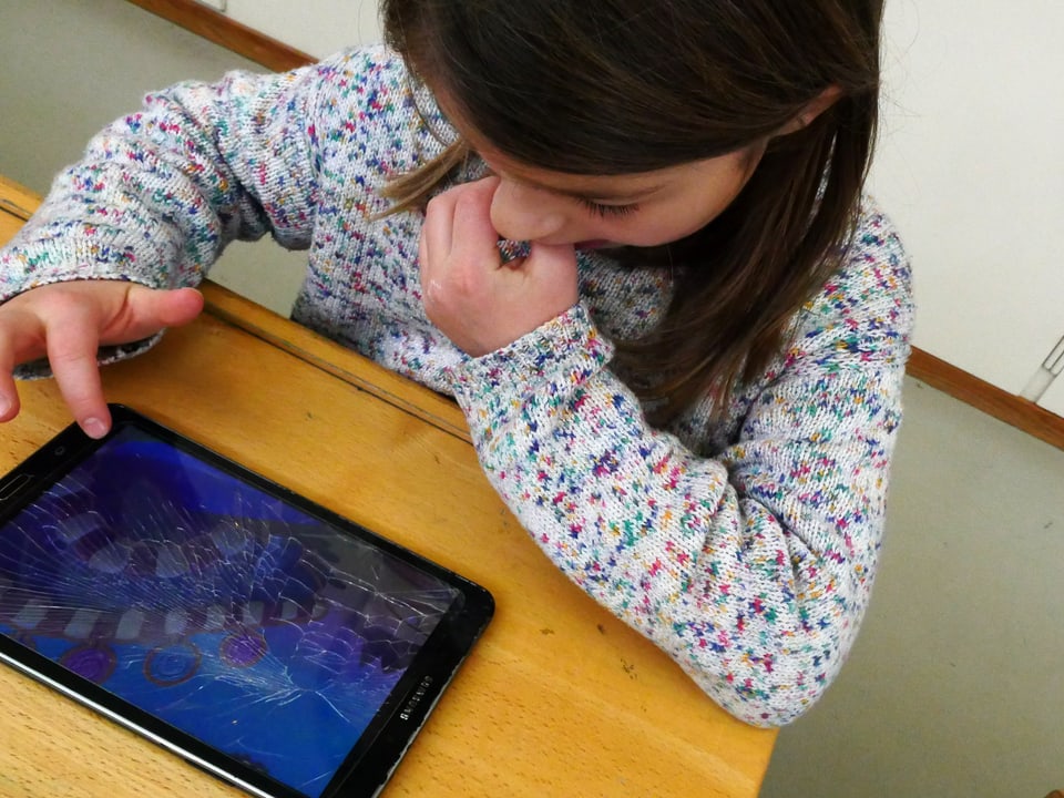 Ein Mädchen spielt mit einem Tablet, dessen Bildschirm zersplittert ist.