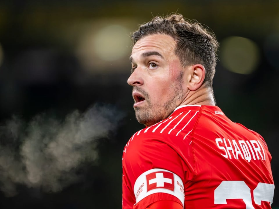 Fussballspieler mit Schweizer Kreuz auf dem Trikot schaut überrascht zur Seite, während Dampf aus seinem Mund steigt.