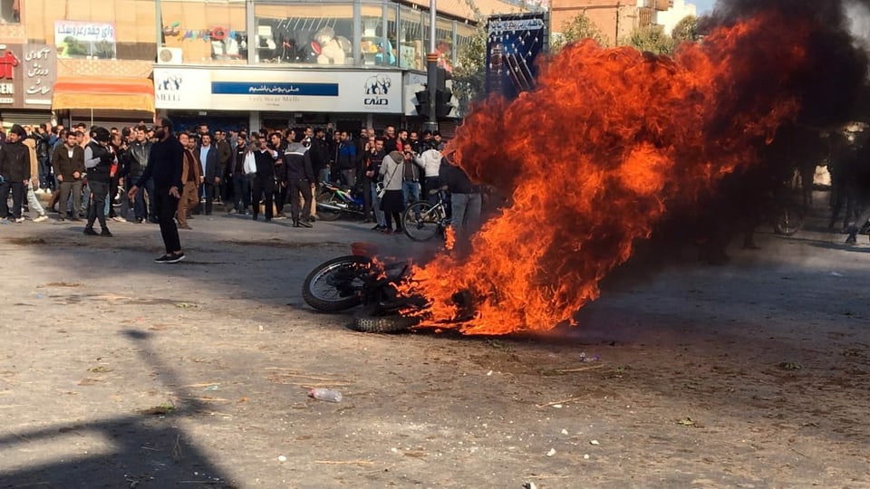Brennendes Motorrad, dahinter eine Menschenmenge.