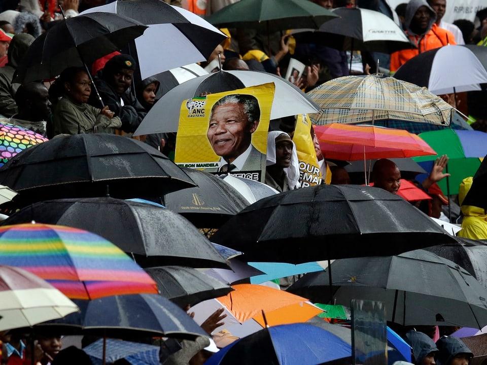 Regenschirme aus denen ein Plakat mit Mandela-Bild herausragt.