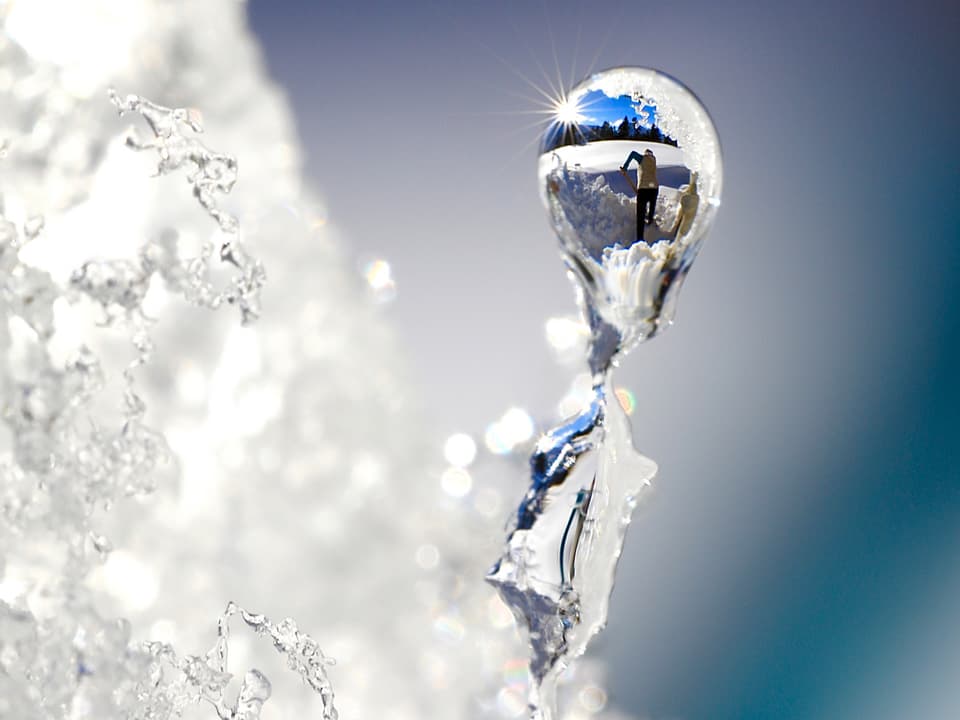 Spiegelbild von einem Schneeschaufelnden in einem Wassertropfen am Schnee