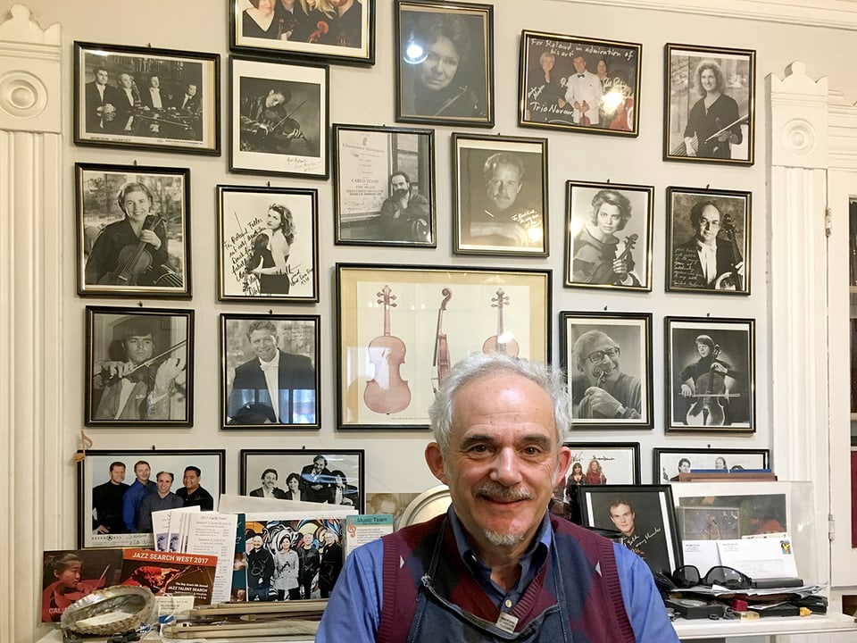 Roland Feller vor einer Wand mit Porträts von Violinisten. 