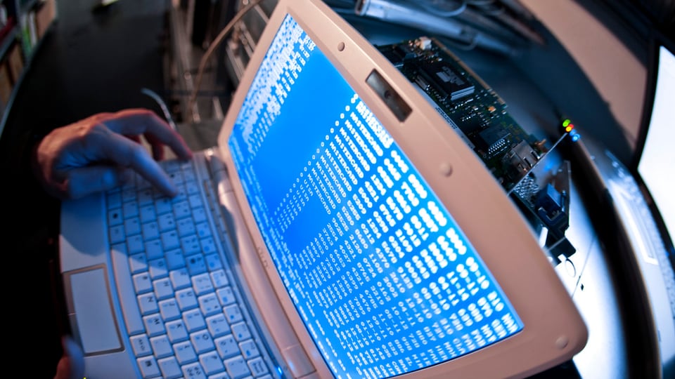 Computer mit blauem Bildschirm, Hand auf Tastatur.