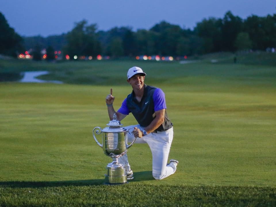 Golfer kniet auf dem Rasen und posiert mit einem grossen Pokal.