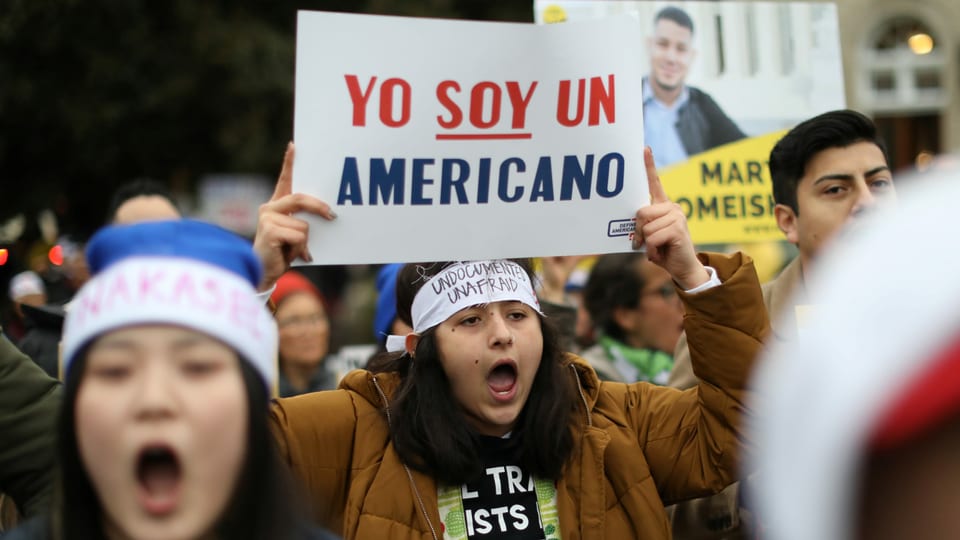 Junge Leute protestieren. Eine hält ein Plakat, darauf steht auf Spanisch: Ich bin eine Amerikanerin.