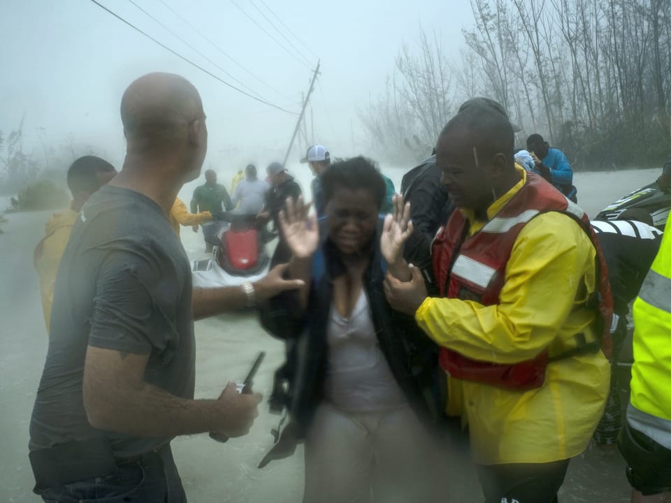 Frau wird bei Überschwemmung und Regen von Helfern begleitet.