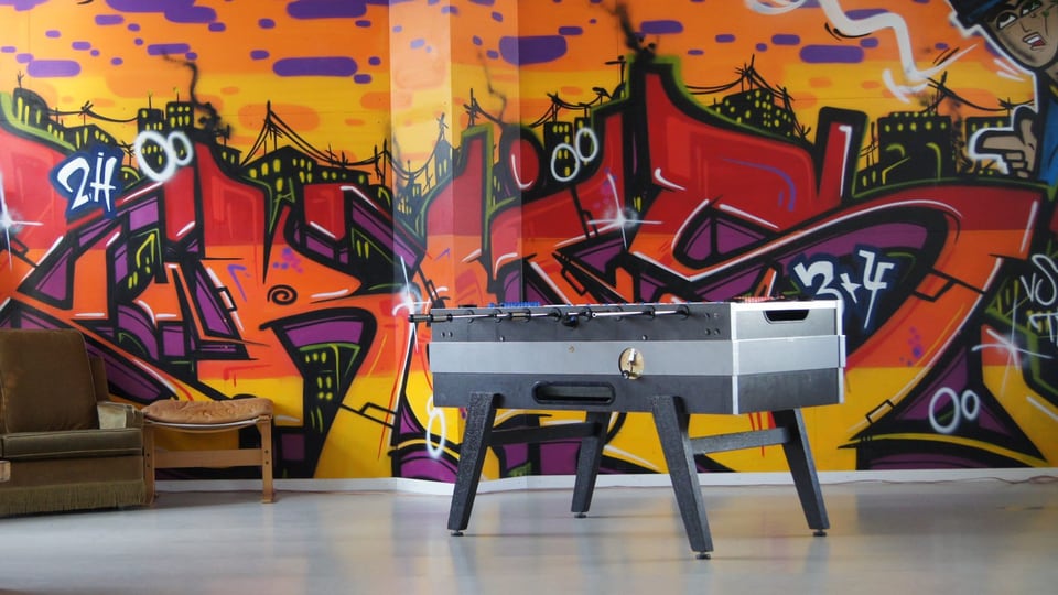 Symbolbild: Ein Tischfussball-Tisch steht vor einer Wand, die mit farbigen Graffiti besprayt ist.