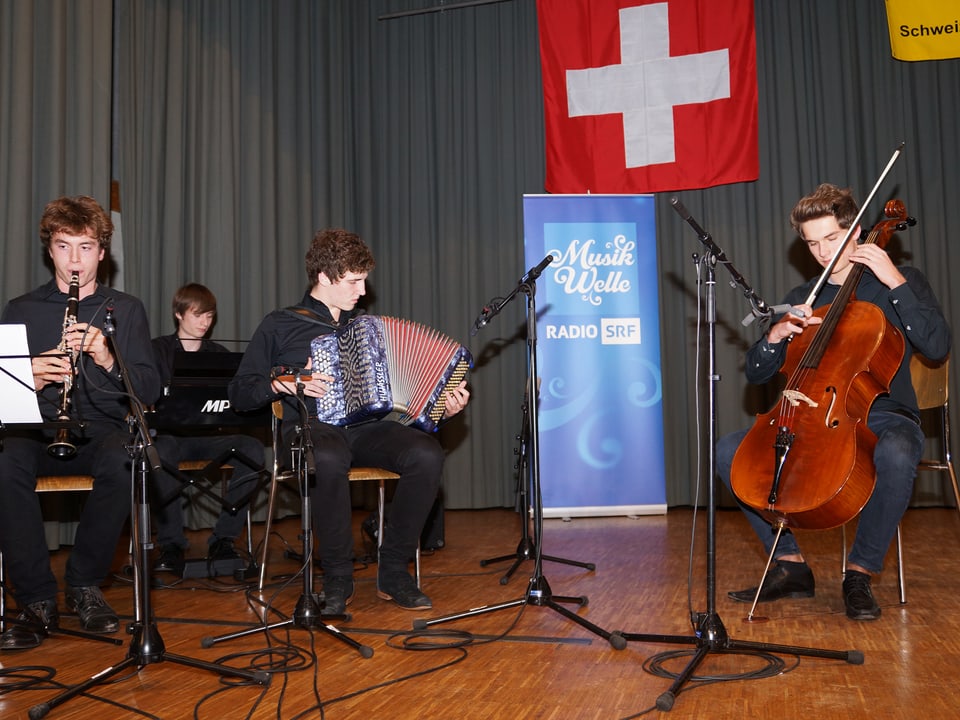 Drei Jungmusikanten mit Klarinette, Akkordeon und Cello auf der Bühne.
