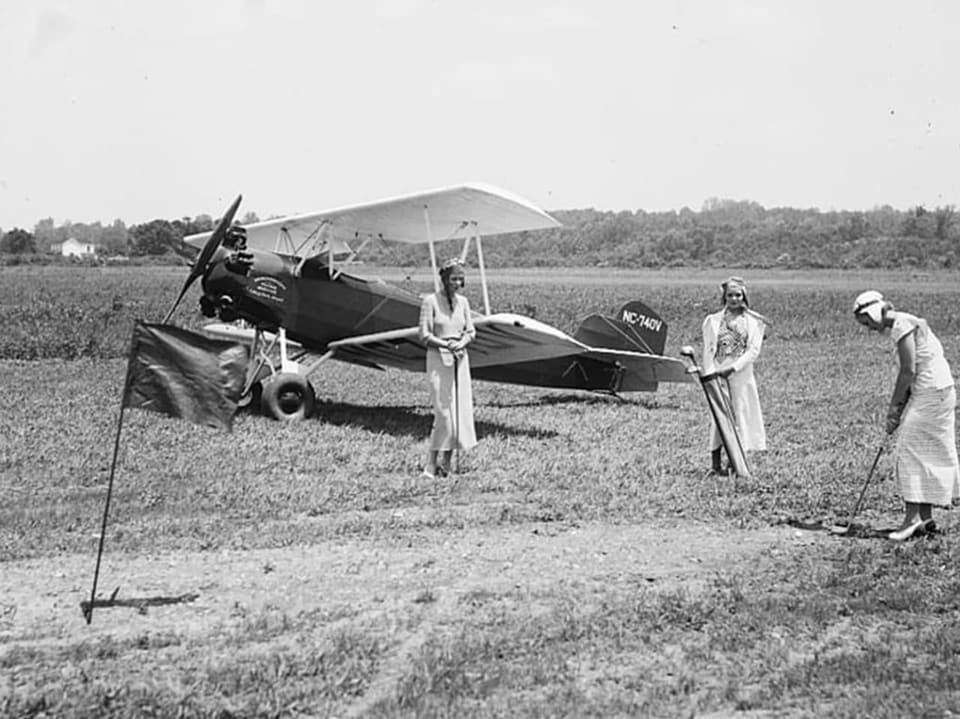 Historisches Foto von drei Personen und einem Kleinflugzeug auf einem Feld