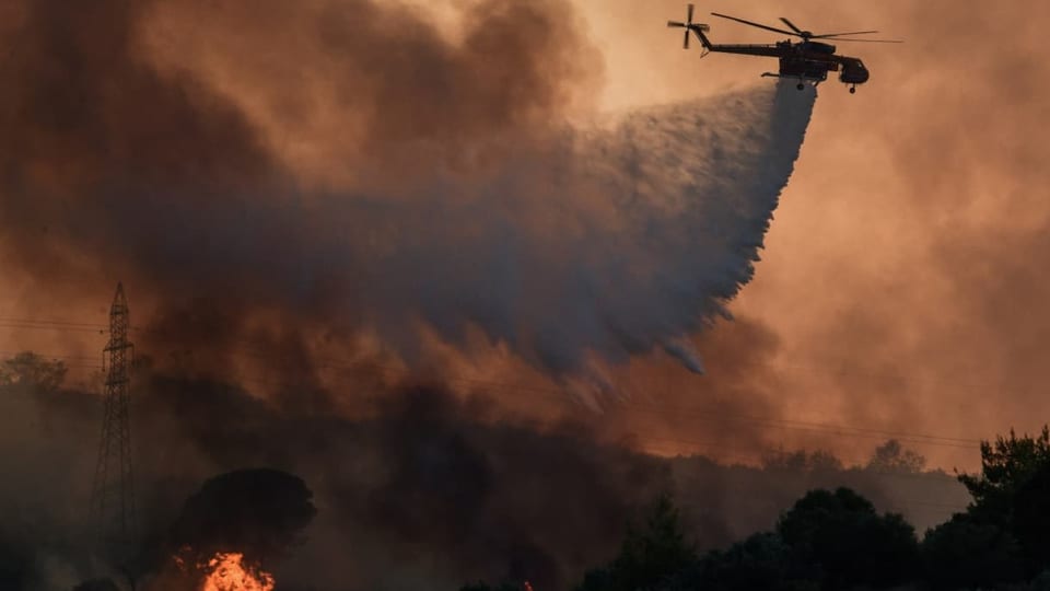 A firefighting helicopter drops water as a forest fire breaks out in the western Peloponnese village of Kresthena.