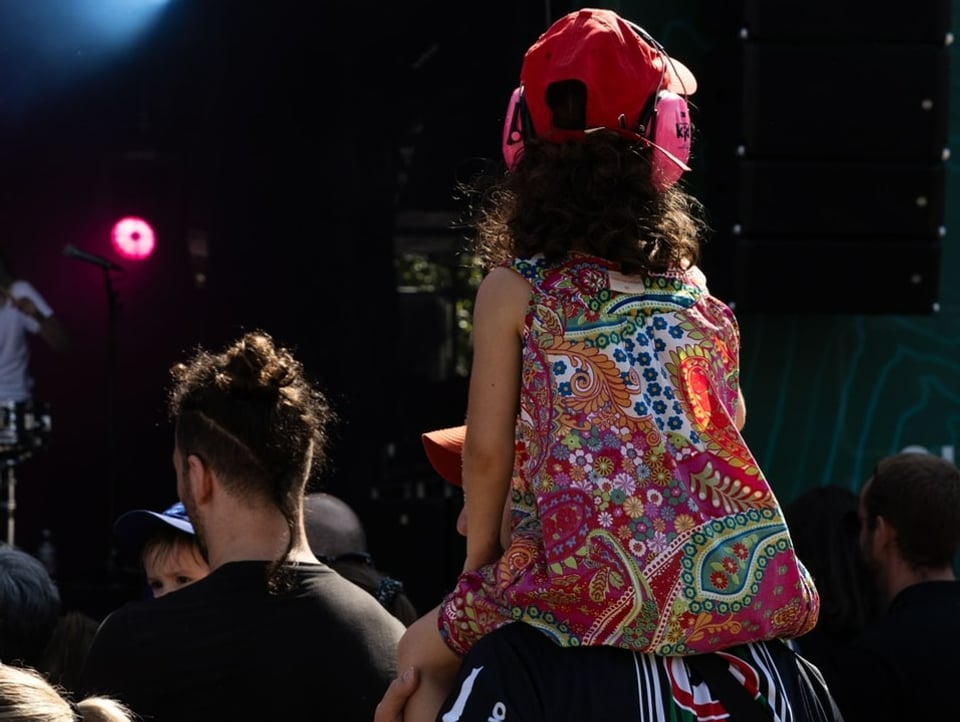 Ein Mädchen sitzt  auf den Schultern einer grösseren Person und schaut auf die Bühne