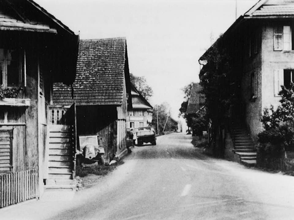 Schwarz-Weiss Fotografie mit einer Strasse, die an alten Häusern vorbeiführt.