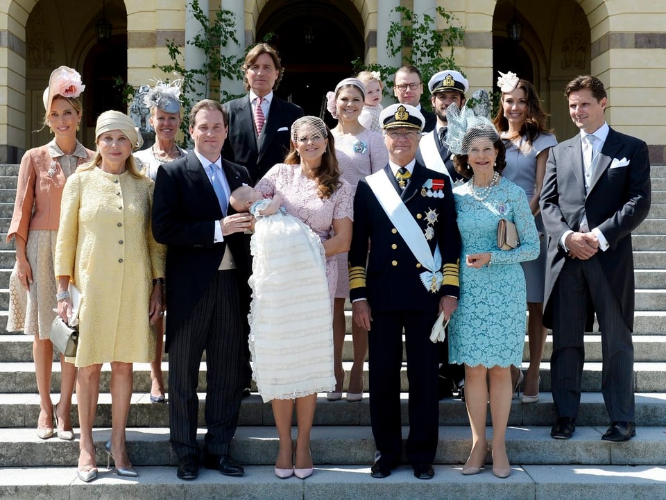 Gruppenfoto der schwedischen Königsfamilie. In der Mitte steht Prinzessin Madeleine mit Baby Leonore im Taufkleidchen auf dem Arm.