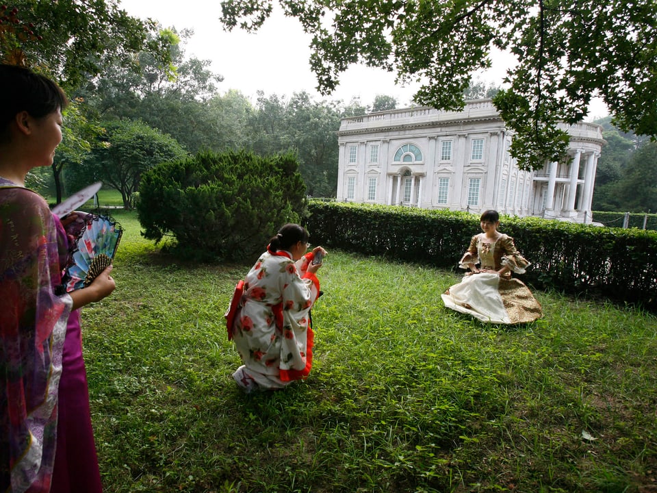 Drei traditionell gekleidete Chinesinnen posieren in Park vor weissem Haus.
