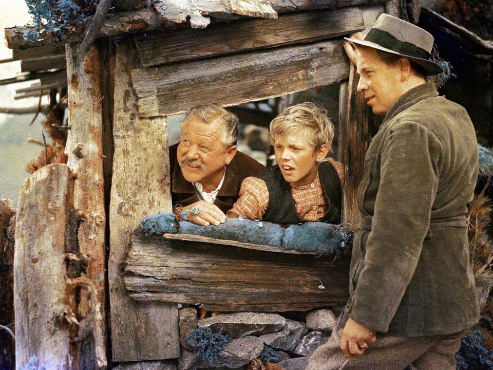 Peter und ein Mann strecken die Köpfe aus einer Hütte und schauen zusammen mit einem weiteren Mann talwärts.