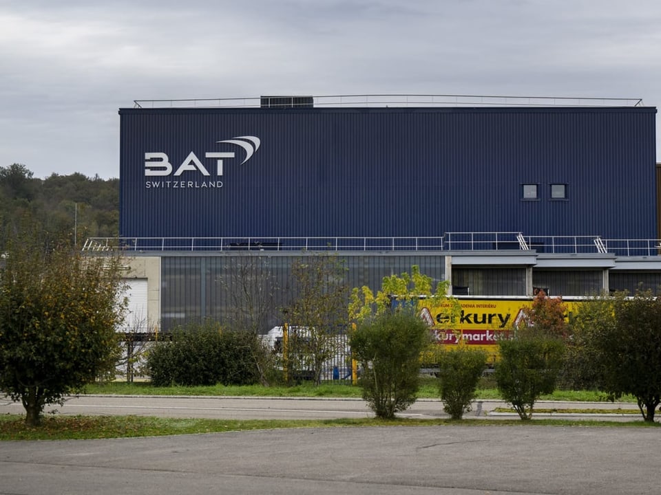 Ein blaues Fabrikgebäude. Auf der Fassade steht der Schriftzug «BAT Switzerland».