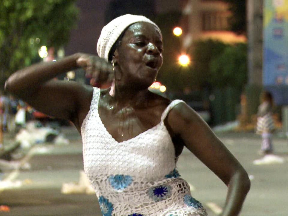 Eine Frau tanzt schweissüberströmt auf der Strasse.