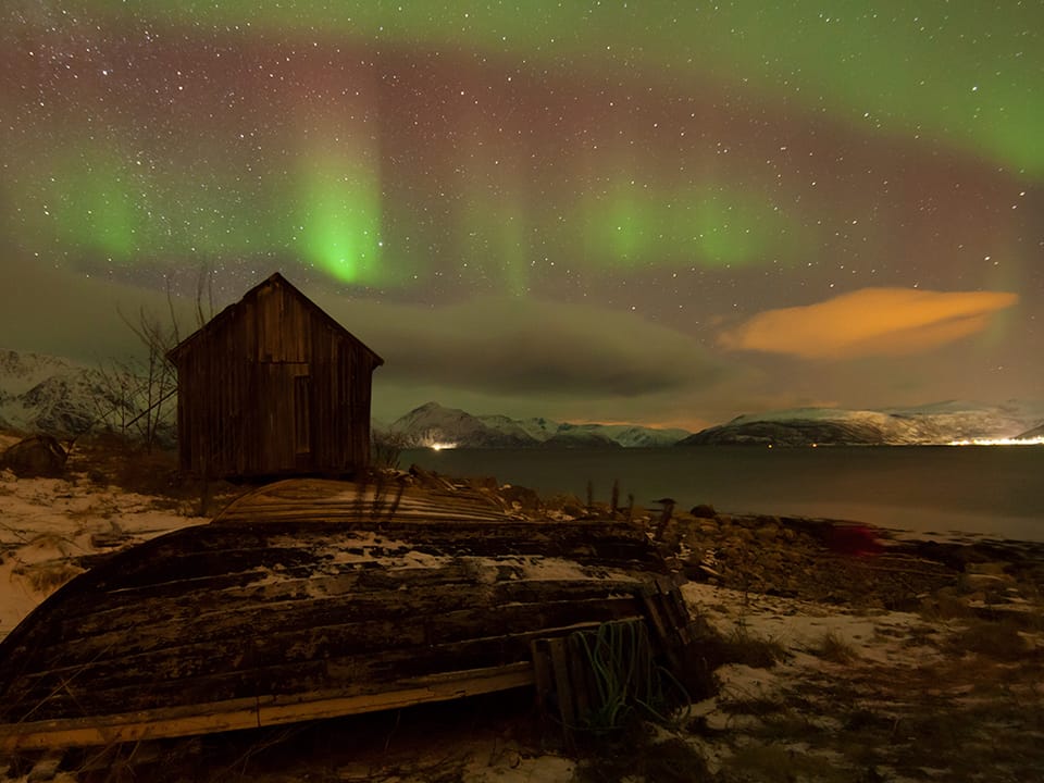 Eine Hütte und ein Holzboot im Licht eines Polarlichts