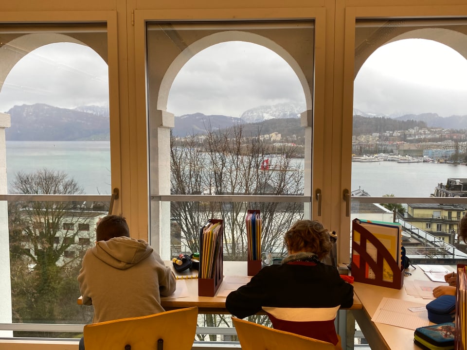 Traumhafte Aussicht 2 Schüler aus der Montessori Schule, die am arbeiten sind. Im Hintergrund ist der Vierwaldstättersee zu sehen.