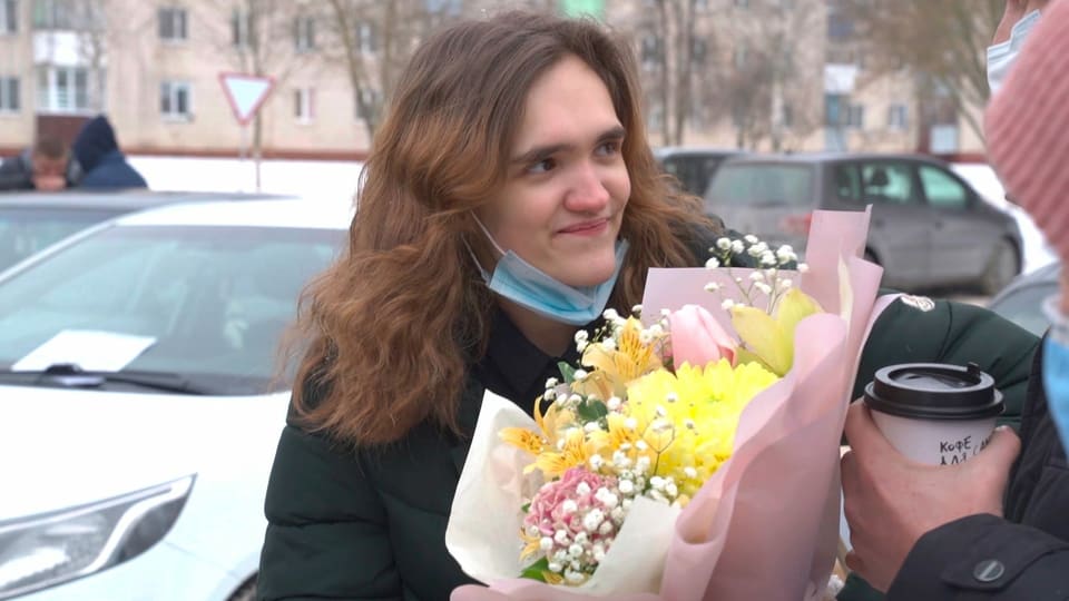 Junge Frau mit Blumenstraus in den Händen blickt lächelnd zur Seite.