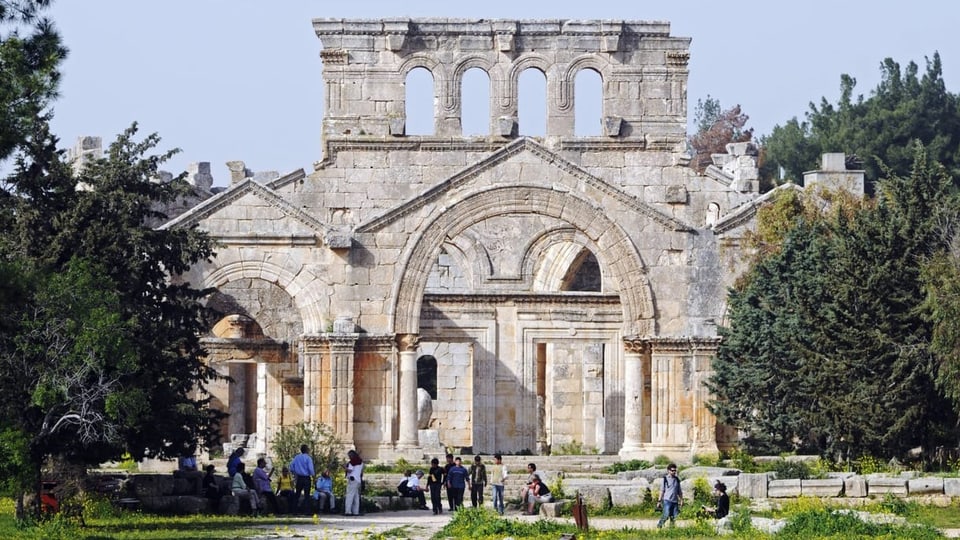 Vor einem steinernen ehemaligen Kloster byzantinischen Stils stehen ein Dutzend Menschen.