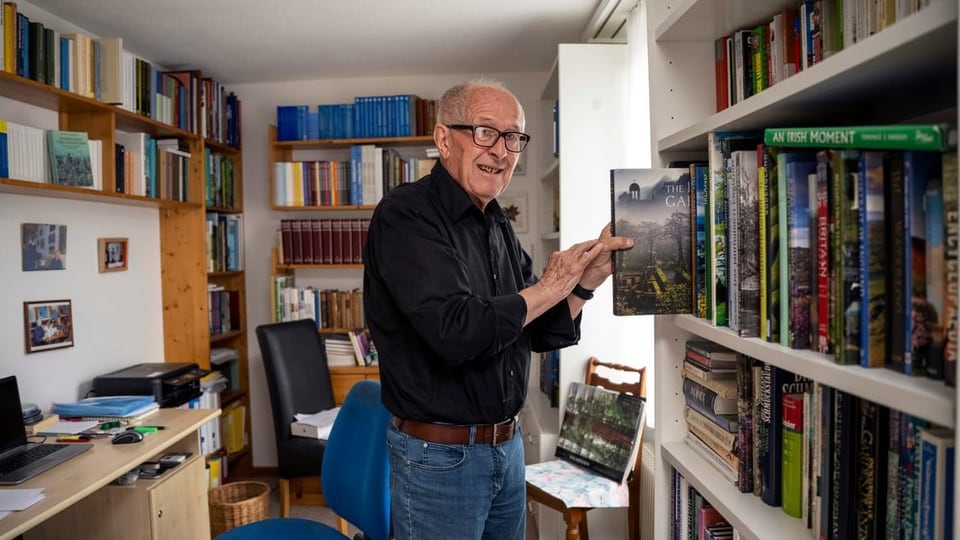 ein älterer Mann steht am Bücherregal