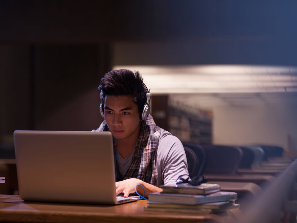 Jugendlicher mit Laptop und Kopfhörer im Lesesaal einer Bibliothek.