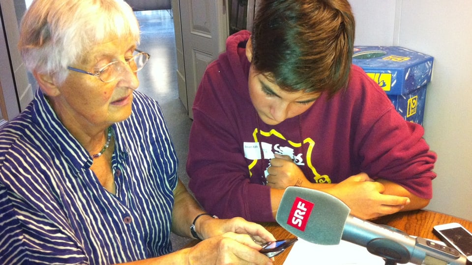 Jugendlicher erklärt Rentnerin ihr Mobiltelefon.
