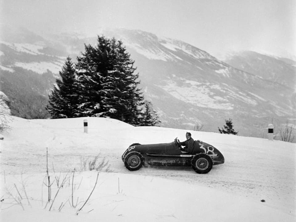 Historische Aufnahme: Einfaches Rennauto ohne Verdeck fährt auf schneebedeckter Strasse