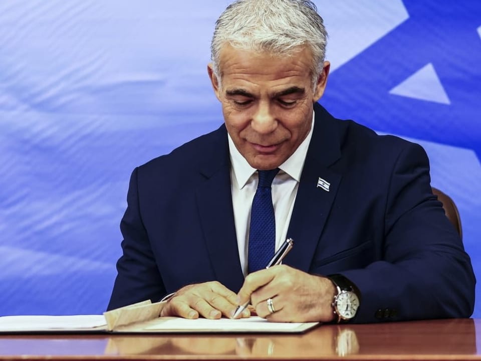 Lapid unterschreibt das Abkommen auf einem Schreibtisch.
