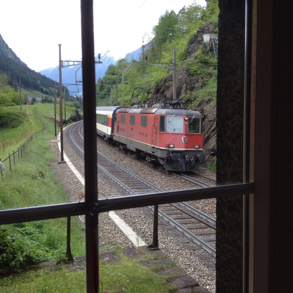 Blick aus Fenster auf Bahnschiene mit roter Lokomotive und Zug. 