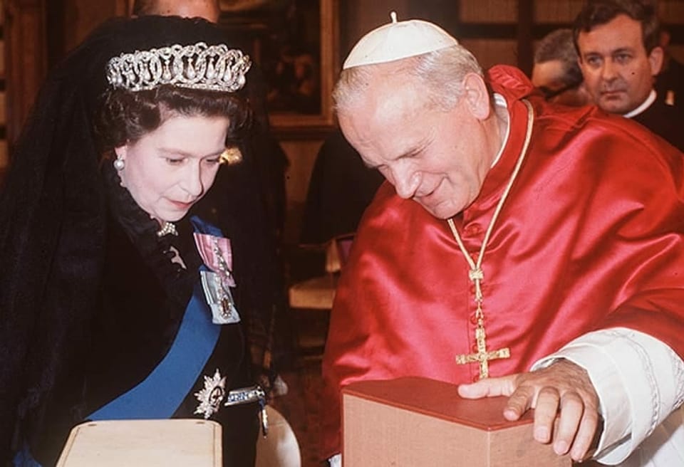 Die Queen mit Diadem trifft den Papst. Er zeigt ihr etwas. Was der Gegenstand ist, ist auf dem Foto nicht ersichtlich.