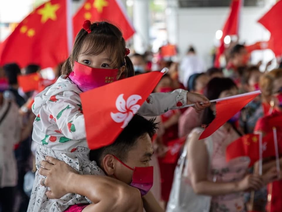 Ein Kind sitzt auf der Schulter eines Mannes (möglicherweise der Vater) und schwenkt die Hongkonger Flagge.
