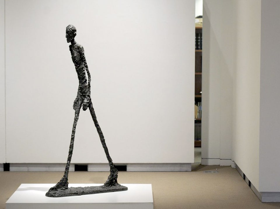 Die Skulptur eines gehenden Mannes auf einem Sockel.