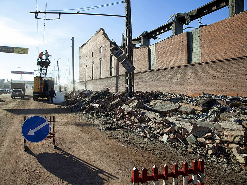 Zerstörte Fassade einer Fabrik, Im Hintergrund arbeiten Elektriker an einer Stromleitung.