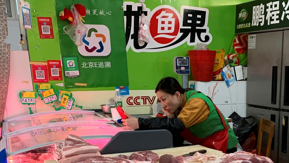 Eine Schweinefleisch-Händlerin schaut auf ihr Smartphone, während sie auf Kunden wartet.