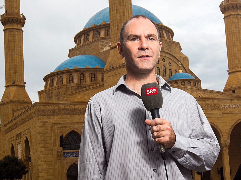 Philipp Scholkmann steht mit Mikrofon vor der Moschee.