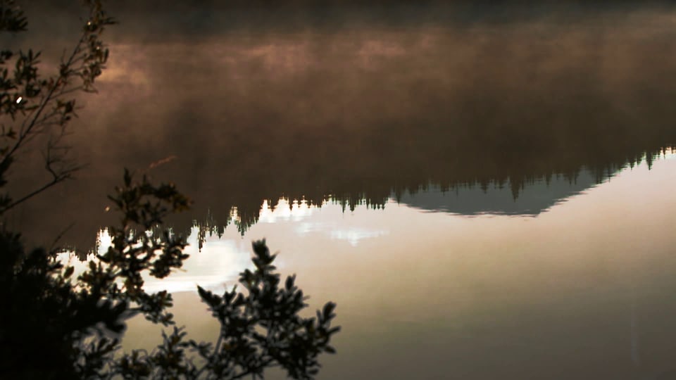 Auf einem See spiegeln sich die Berge in der Abendstimmung. 