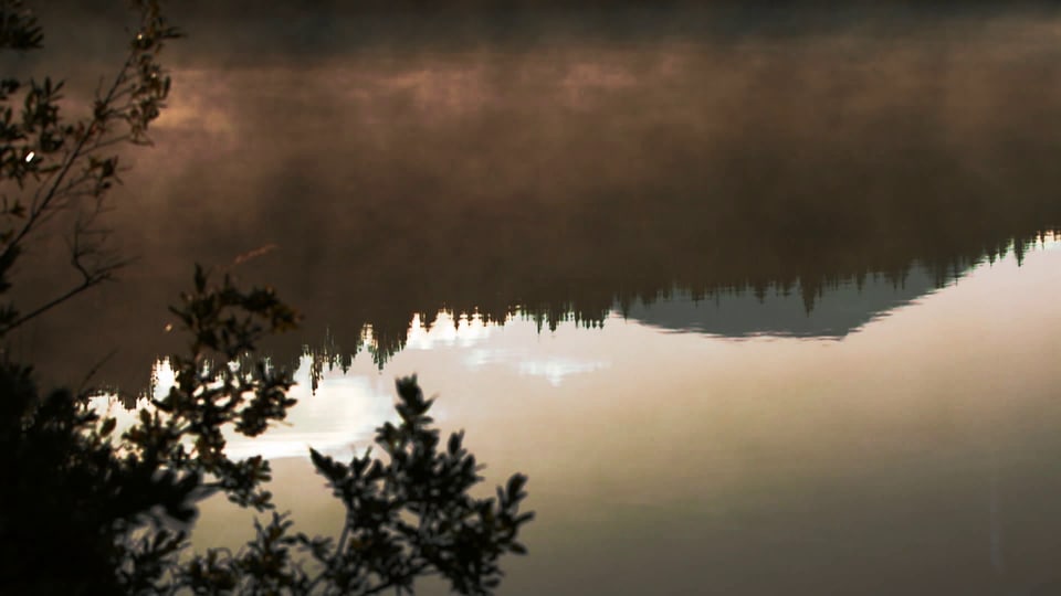 Auf einem See spiegeln sich die Berge in der Abendstimmung.