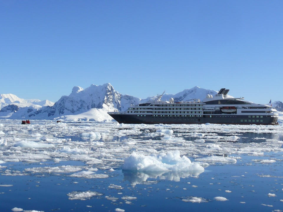 Zwischen Eisbergen ist ein grösseres Schiff vor Anker, ein kleineres ist unterwegs ans Ufer.