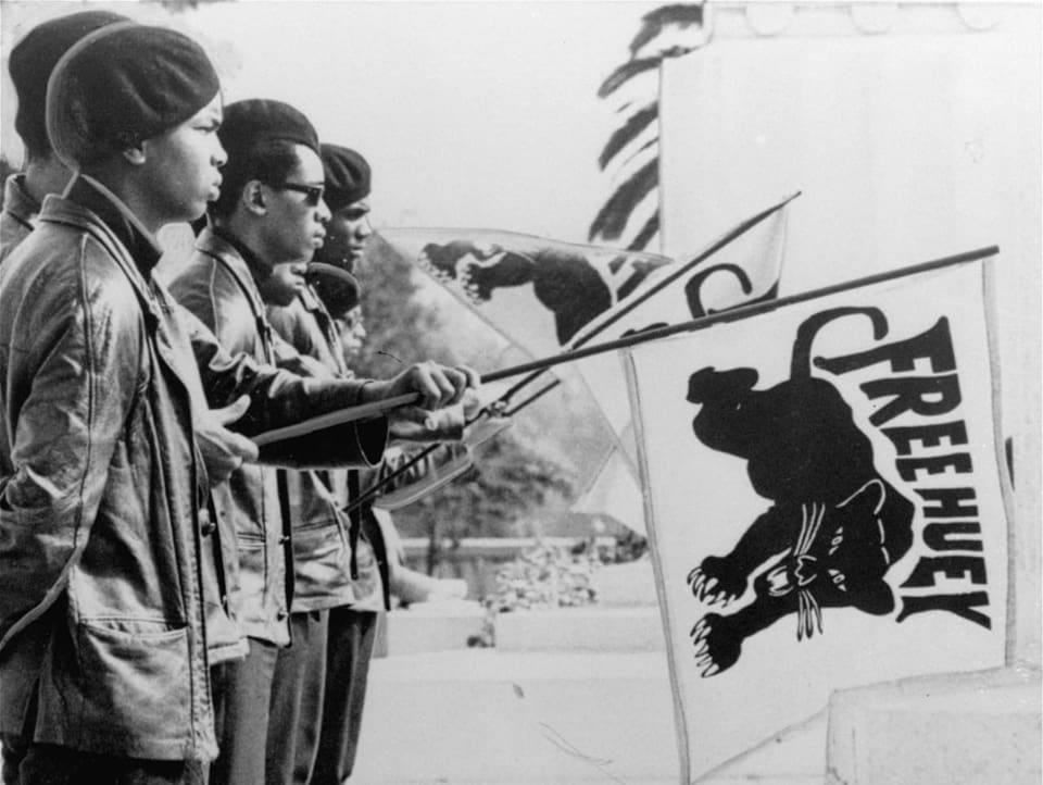 Schwarze Männer halten eine Flagge mit einem schwarzen Panther und der Aufschrift «Free Huey».